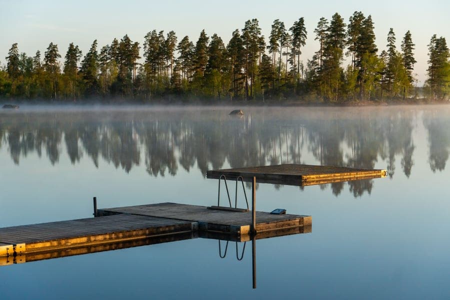 Wooden docks on a calm, misty lake at dawn, with pine trees reflected in the water
