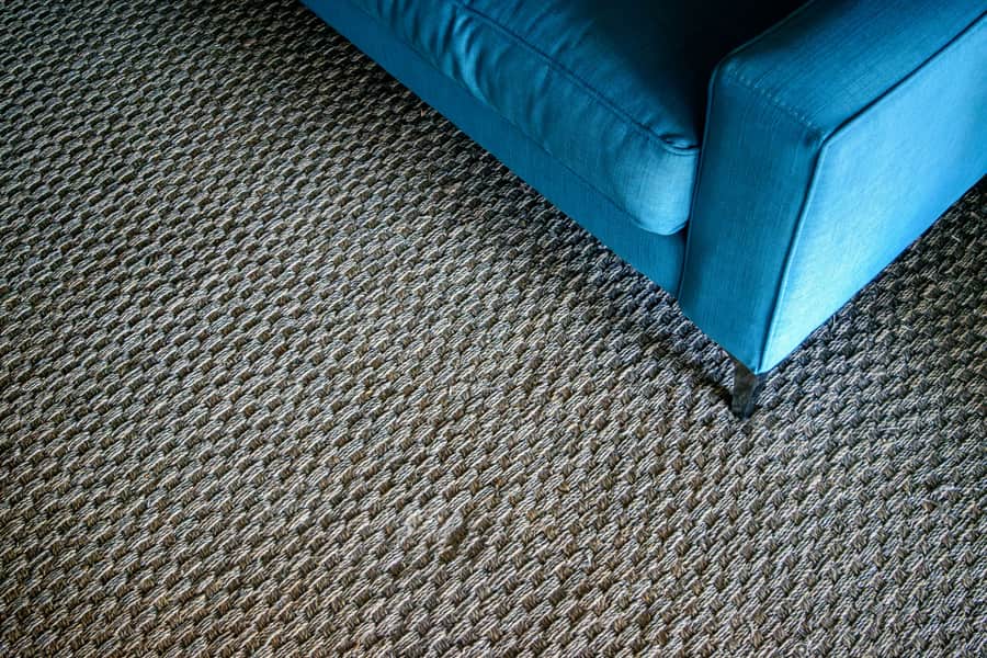 The corner of a blue sofa resting on a textured woven rug
