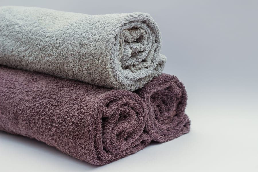 Rolled gray and mauve bath towels stacked on a white surface