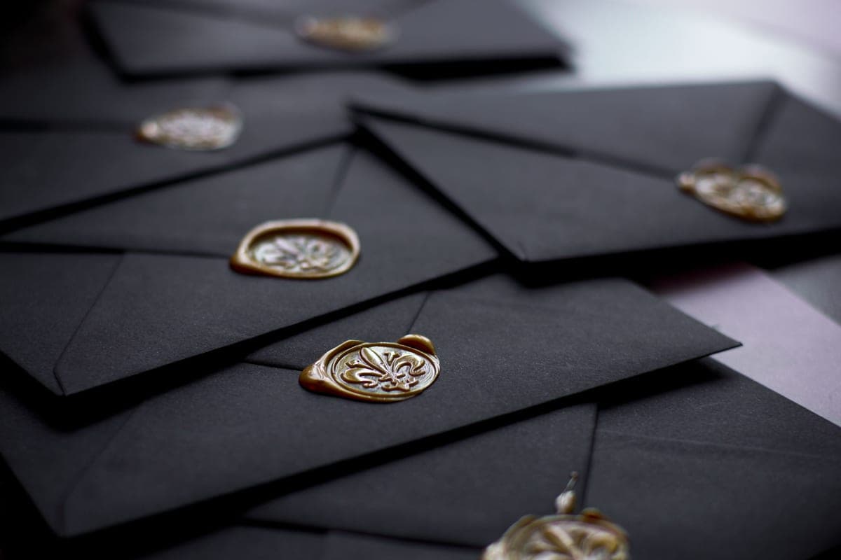 Black envelopes closed with gold wax seals, stacked on a dark surface